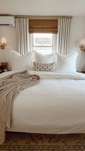 A neatly made bed with white linens and decorative pillows, a patterned throw blanket, and a window with blinds. - Charming 1940s cottage near college and downtown (Caldwell)