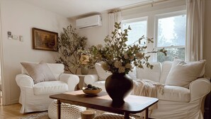 Un salon avec deux canapés blancs, une table basse en bois sur laquelle est posé un vase de fleurs, un tapis à motifs et un tableau accroché au mur.
