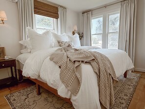 A bedroom with a large bed, a bedside table, a lamp, and a window with curtains. - Charming 1940s cottage near college and downtown (Caldwell)