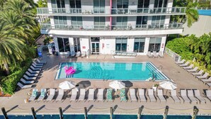 A modern hotel with a large pool, sun loungers, and a palm tree-lined deck. - Waterfront Condo 2BR  Intracoastal Marina (Hallandale Beach)