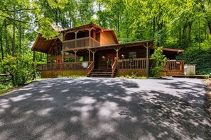 Ein zweistöckiges Holzblockhaus mit Balkon, einer Veranda und einer Auffahrt, die zum Eingang führt.