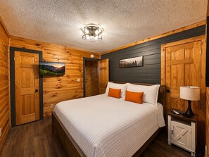 A bedroom with a bed, a nightstand, a lamp, a TV, and a door. - 3BR w/Hot Tub*Games*Privacy*15 mins to Dollywood (Sevierville)