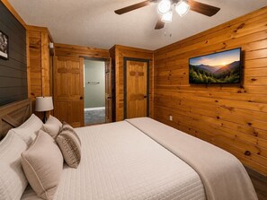 Ein Schlafzimmer mit einem Bett, Kissen, einer Lampe, einem Deckenventilator und einem Bild an der Wand.