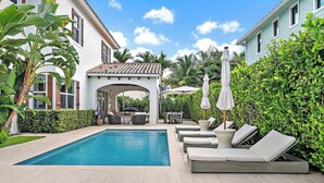 A swimming pool with lounge chairs and umbrellas, surrounded by greenery and a pergola. - 4BR Private Family Compound Heart of Delray Beach (Delray Beach)