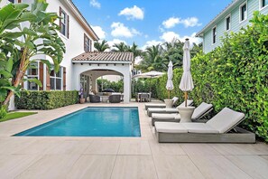 Ein Pool mit Liegestühlen und Sonnenschirmen, umgeben von Grünflächen und einer Pergola.