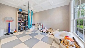 A child's playroom with a checkered floor, a basketball hoop, a hanging hammock, and a large window. - 4BR Private Family Compound Heart of Delray Beach (Delray Beach)