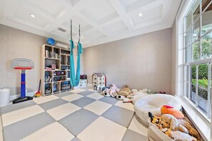 Ein Kinderzimmer mit Schachbrettmuster auf dem Boden, einem Basketballkorb, einer Hängematte und einem großen Fenster.
