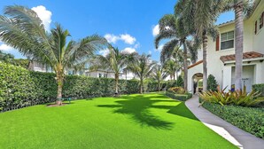 A well-maintained lawn with palm trees and a pathway leading to a building with a tiled roof. - 4BR Private Family Compound Heart of Delray Beach (Delray Beach)