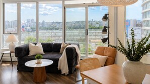 Een moderne woonkamer met een groot raam, een donkere bank, een ronde salontafel, een eettafel met stoelen en een hanglamp.