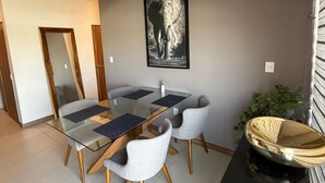 Un comedor con una mesa de vidrio, cuatro sillas grises, un cuadro con una imagen de elefante y un cuenco decorativo sobre un mueble negro.