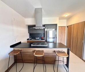 A modern kitchen with a central island, bar stools, a stove, and a refrigerator. - Lovely Guadalajara (Zapopan)