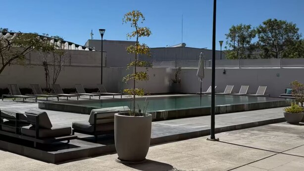 Un área de piscina en la azotea con sillones reclinables, una jardinera grande con un árbol y una farola.