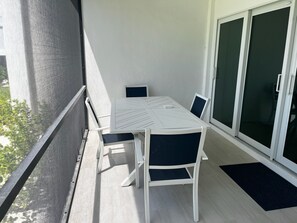 A balcony with a table and chairs, a sliding glass door, and a view of greenery. - Newly remodeled Beachfront 2BR-2Bath Condo / Pool & Gulf Views (Fort Myers Beach)