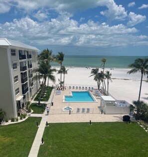 A hotel with a pool, beach, and palm trees. - Newly remodeled Beachfront 2BR-2Bath Condo / Pool & Gulf Views (Fort Myers Beach)