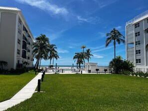 Ein Hotelinnenhof mit blauem Himmel, Palmen, einem Poolbereich und einem weißen Gebäude mit Balkonen.