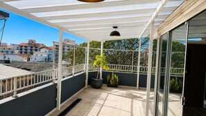 A covered balcony with a potted plant, a black pendant light, and a view of buildings in the background. - Penthouse with ocean view, one block from the beach, with private garage. (Florianópolis)