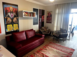 Ein Wohnzimmer mit einem roten Sofa, einem gemusterten Sessel und einem Bücherregal voller Bücher und Poster.