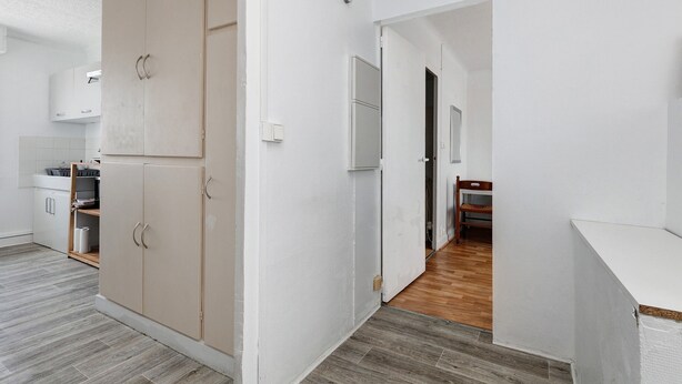 A modern kitchen with white cabinets, a wooden floor, and a view into the dining area. - Hoedic – Apartment for 6 Guests with Wi-Fi (Le Croisic)