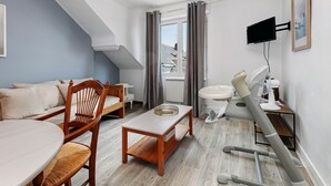A compact hotel room with a bed, a small table, a chair, a desk with a chair, a television, and a bathroom with a sink and toilet. - Hoedic – Apartment for 6 Guests with Wi-Fi (Le Croisic)
