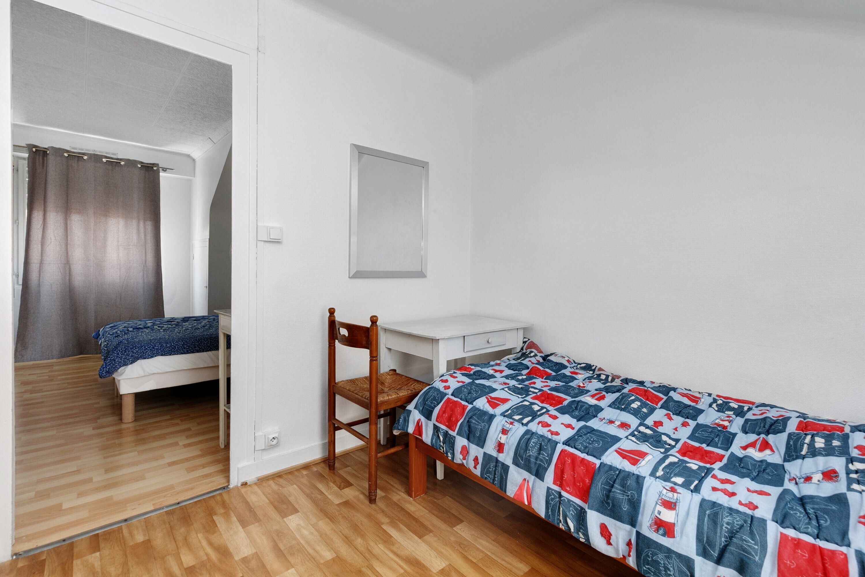 A single-bed room with a wooden floor, a desk, a chair, and a bed with a patterned bedspread.