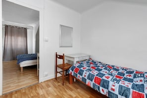 A single-bed room with a wooden floor, a desk, a chair, and a bed with a patterned bedspread.