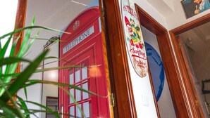 Uma cabine telefônica vermelha com uma placa que diz 'TELEPHONE' e uma prancha de surf com a inscrição 'Surfing Forever' ao fundo.
