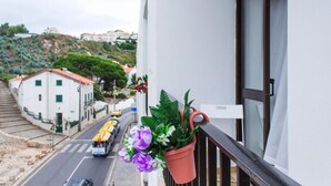 Uma varanda com um vaso de planta e vista para uma rua com bondes.
