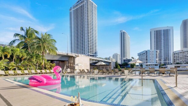 A swimming pool with lounge chairs and palm trees, surrounded by tall buildings. - 1BR  Intracoastal View - Resort & Pool (Hallandale Beach)