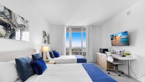 Ein Hotelzimmer mit zwei Betten, einem Schreibtisch, einem Fernseher und Blick auf die Stadt.