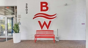 Ein Gebäudeeingang mit einer roten Bank, einem großen Logo mit den Buchstaben 'B' und 'W' und der Zahl '2602' an der Wand.