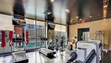 Ein modernes Fitnessstudio mit Cardiogeräten, Kurzhanteln und Blick auf eine Stadtkulisse durch große Fenster.