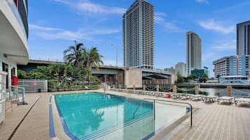 Ein Pool auf dem Dach mit Blick auf hohe Gebäude, Palmen und eine Uferpromenade.