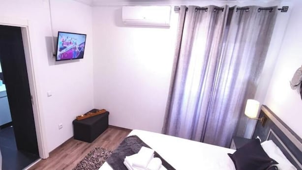 A bedroom with a bed, a flat-screen TV mounted on the wall, a small wooden stool, and a curtain. - Casa da Floresta (Covilha)