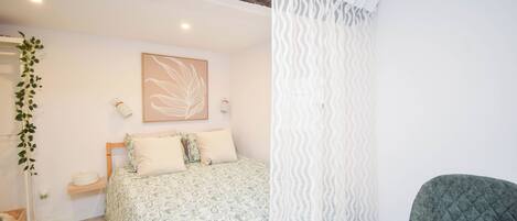 A bedroom with a bed, a bedside table, a chair, a wall-mounted shelf, and a hanging plant.
