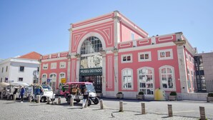 A pink building with a sign reading 'MUSEU DO FADO' and a street vendor area in front. - Alma D'Alfama (Lisboa)