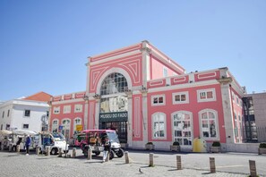 A pink building with a sign reading 'MUSEU DO FADO' and a street vendor area in front. - Alma D'Alfama (Lisboa)