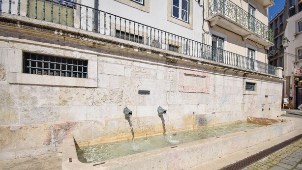 A stone wall with a rectangular water feature, a metal railing, and a window with a barred design. - Alma D'Alfama (Lisboa)