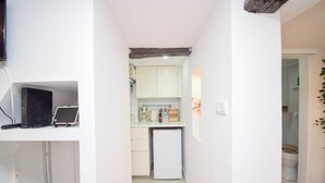 A narrow hallway leading to a kitchen with white cabinets, a small refrigerator, and a laptop on a shelf. - Alma D'Alfama (Lisboa)