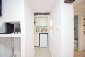A narrow hallway leading to a kitchen with white cabinets, a small refrigerator, and a laptop on a shelf. - Alma D'Alfama (Lisboa)