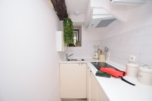 A kitchen with white cabinets, a sink, a countertop with a red bag, and a hanging plant. - Alma D'Alfama (Lisboa)