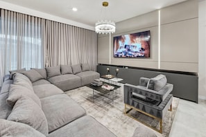 A modern living room with a sectional sofa, a coffee table, a side table, and a television mounted on the wall. - 10BR house with game room near Disney area (Davenport)