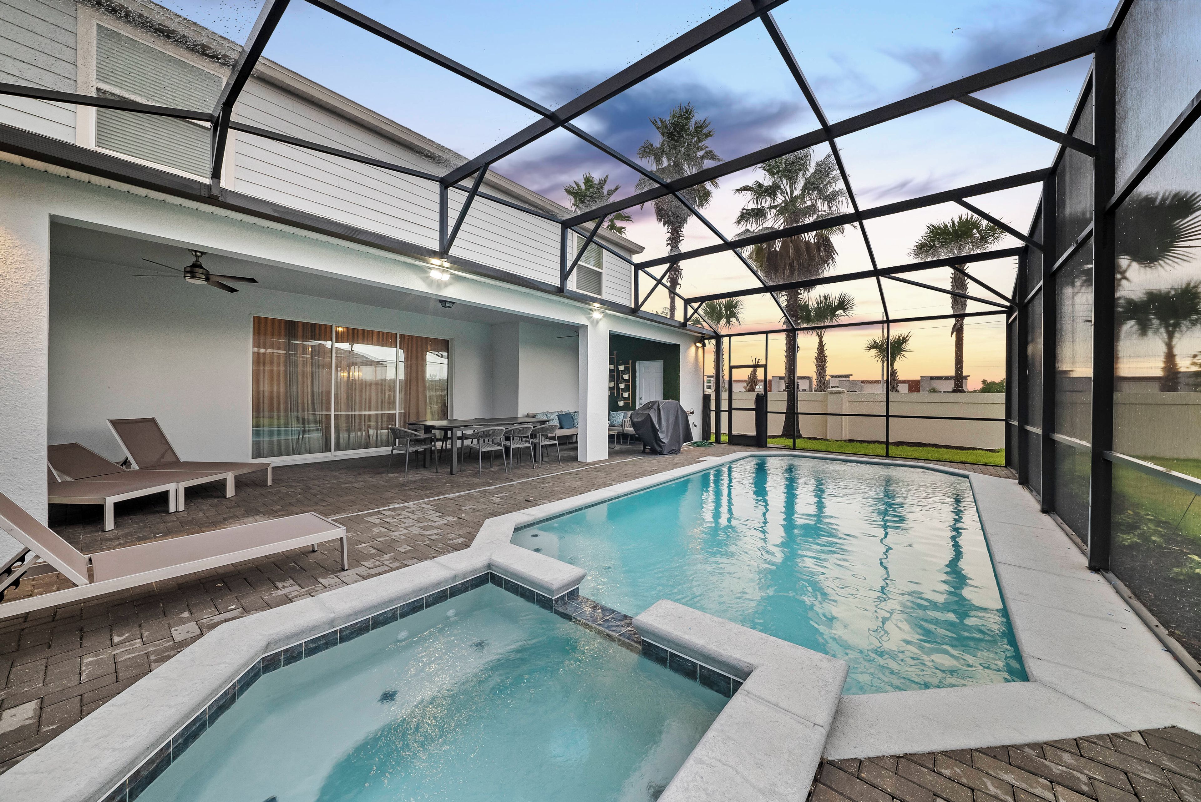 A pool area with a covered patio, lounge chairs, and a view of palm trees.