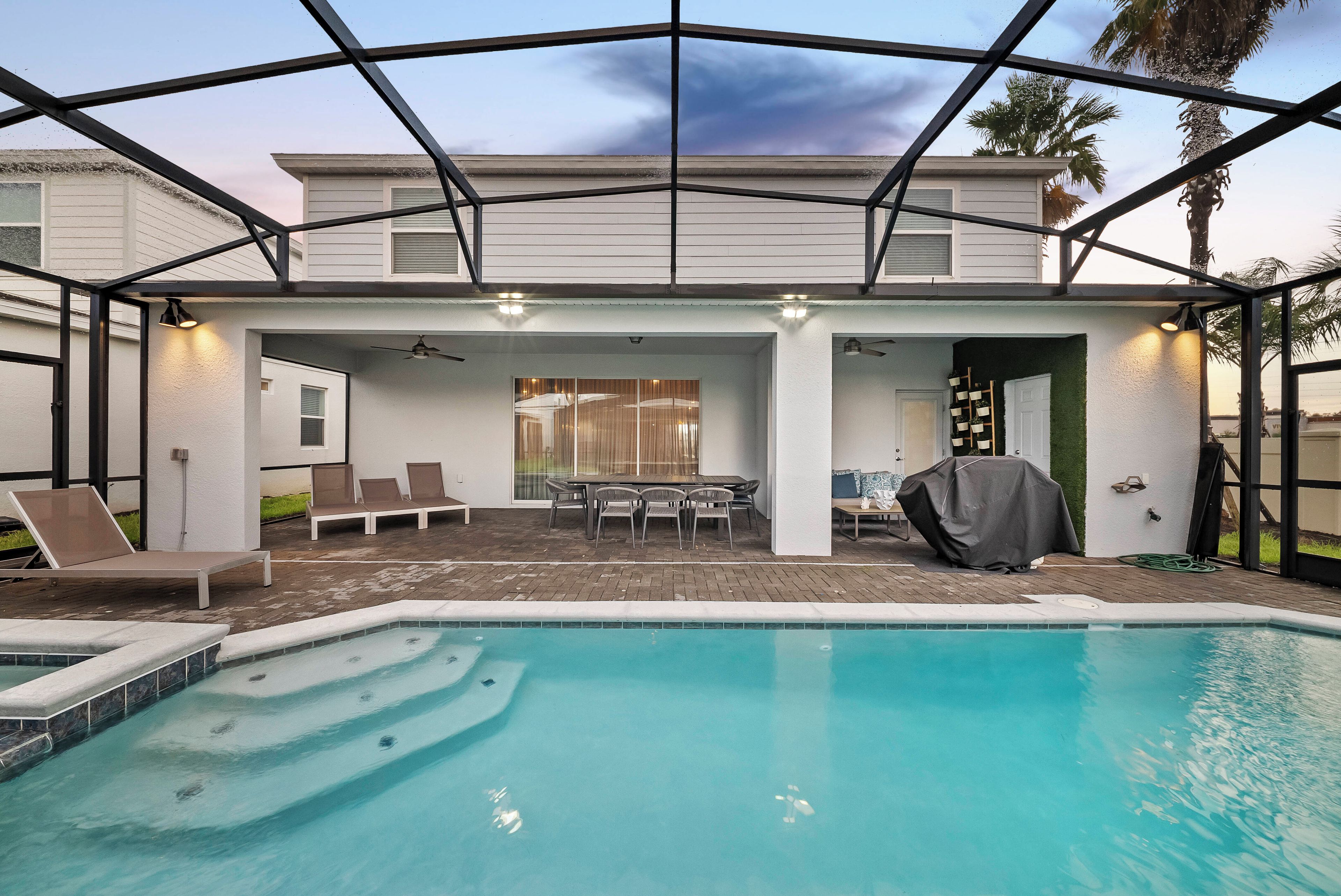 Et overdækket udendørs område med swimmingpool, siddepladser og et terrassebord.