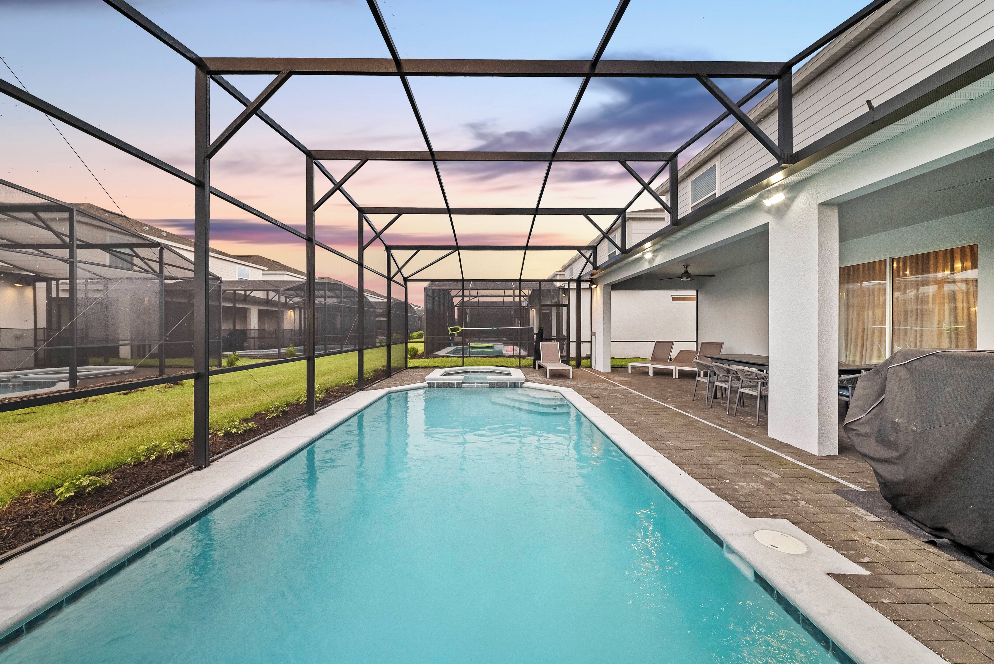 A swimming pool with a covered patio area, surrounded by a fence, and a view of a residential building in the background.
