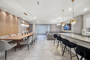 Une cuisine moderne dotée d’un grand îlot central, un coin repas avec une longue table et un espace de vie avec un canapé.