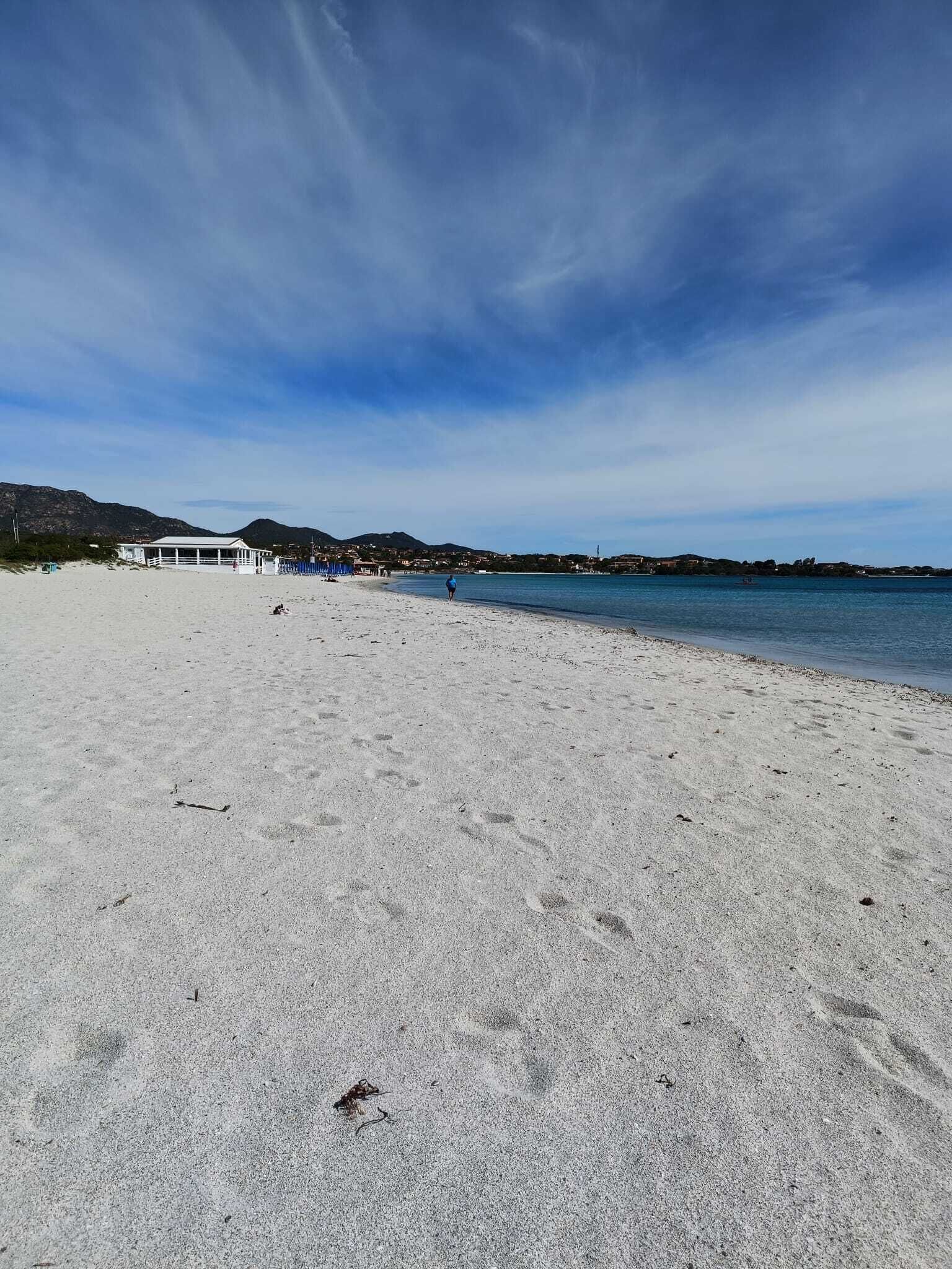 En strand med klart skys og sandet bred, samt en bygning i baggrunden.