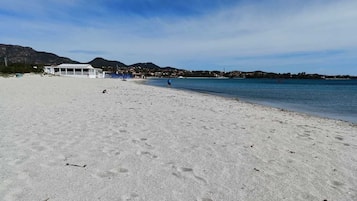 En strand med klart skys og sandet bred, samt en bygning i baggrunden.