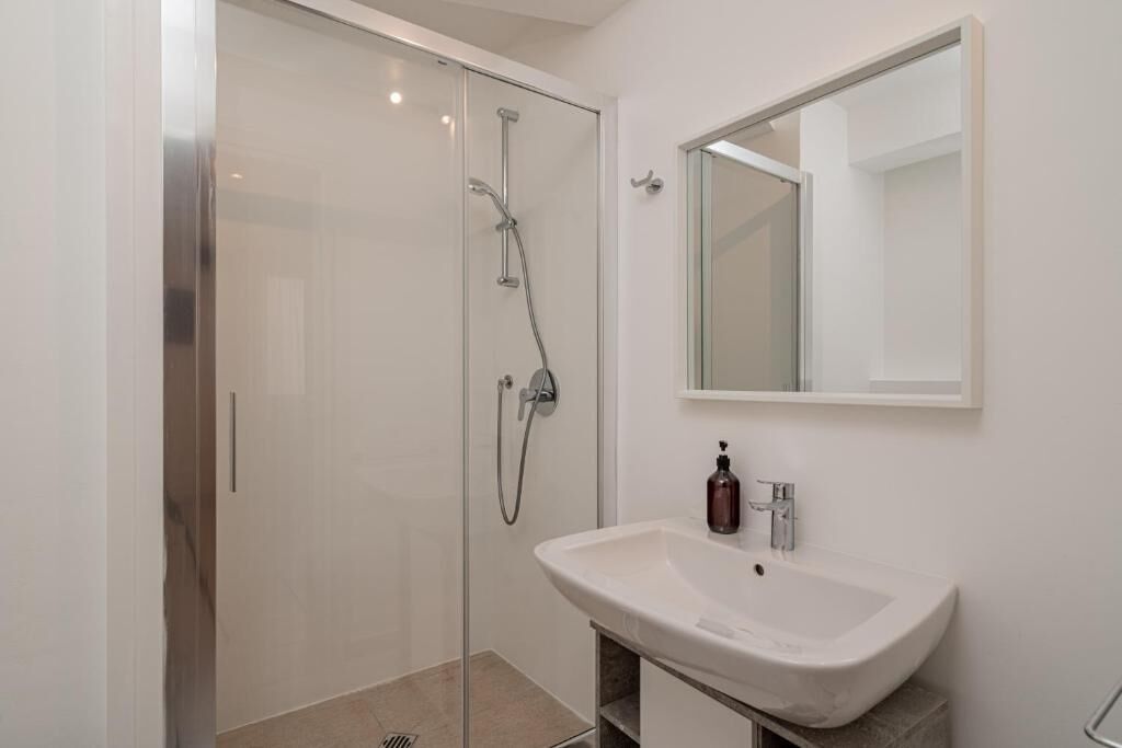 Un baño moderno con cabina de ducha de vidrio, un lavabo blanco y un espejo sobre él.