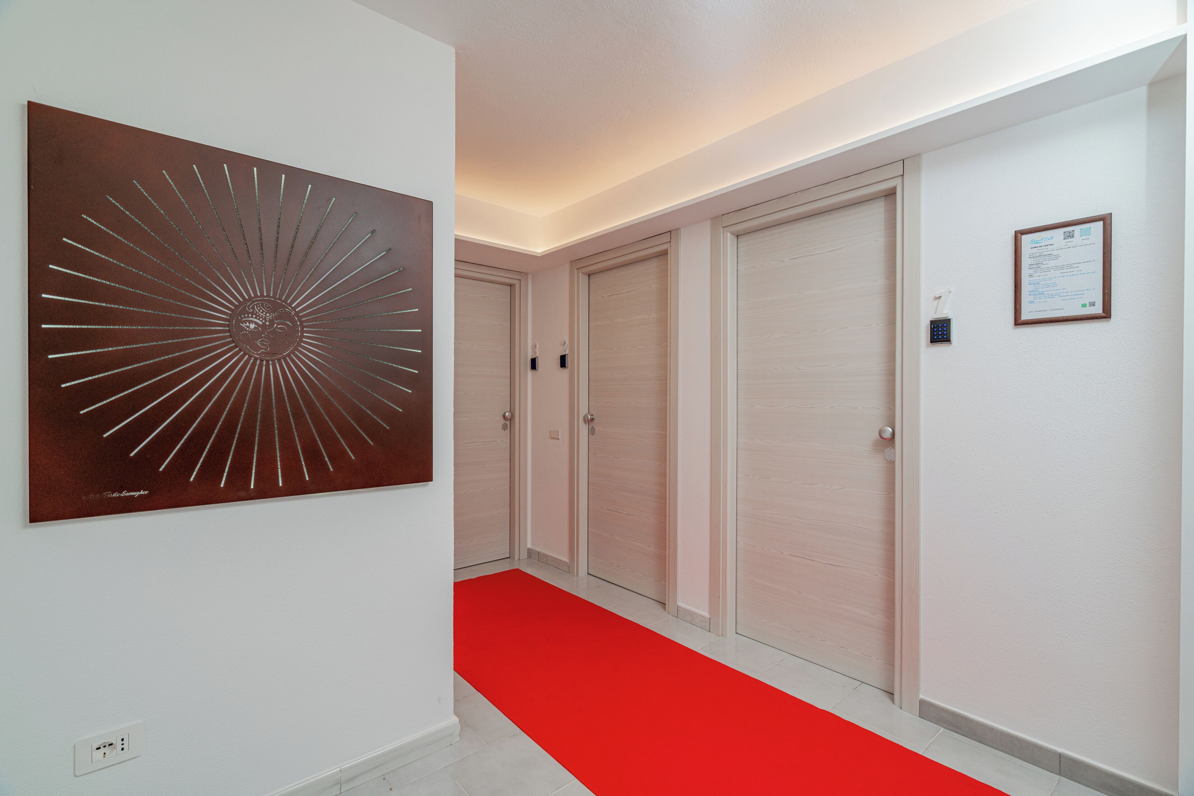 Un pasillo con alfombra roja, una obra de arte en la pared y una puerta con cerradura electrónica.