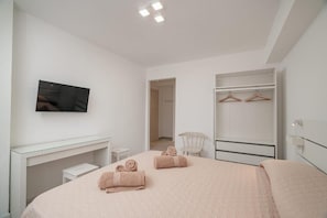 Quarto de hotel moderno com cama, televisão, escrivaninha e guarda-roupa.